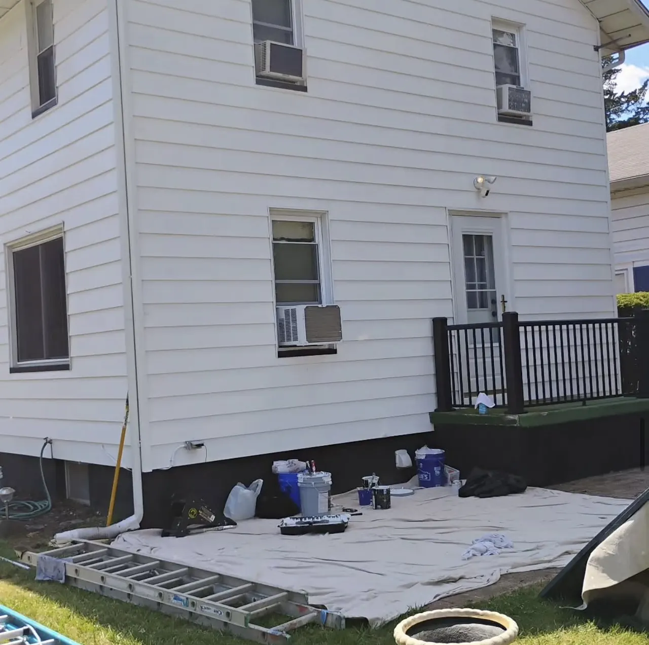 White siding house mid repaint with drop cloths down